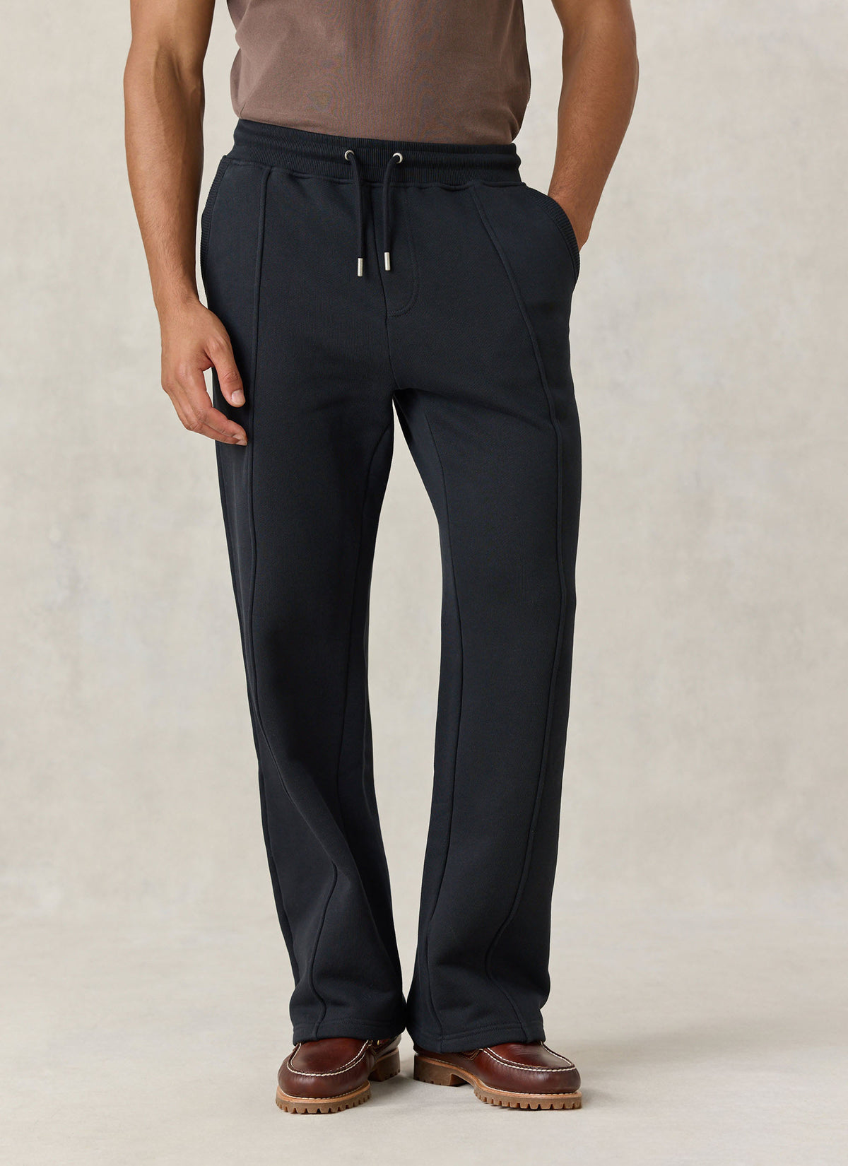 A model wearing Percival black straight leg trackpants in organic cotton jersey with stitched front creases.
