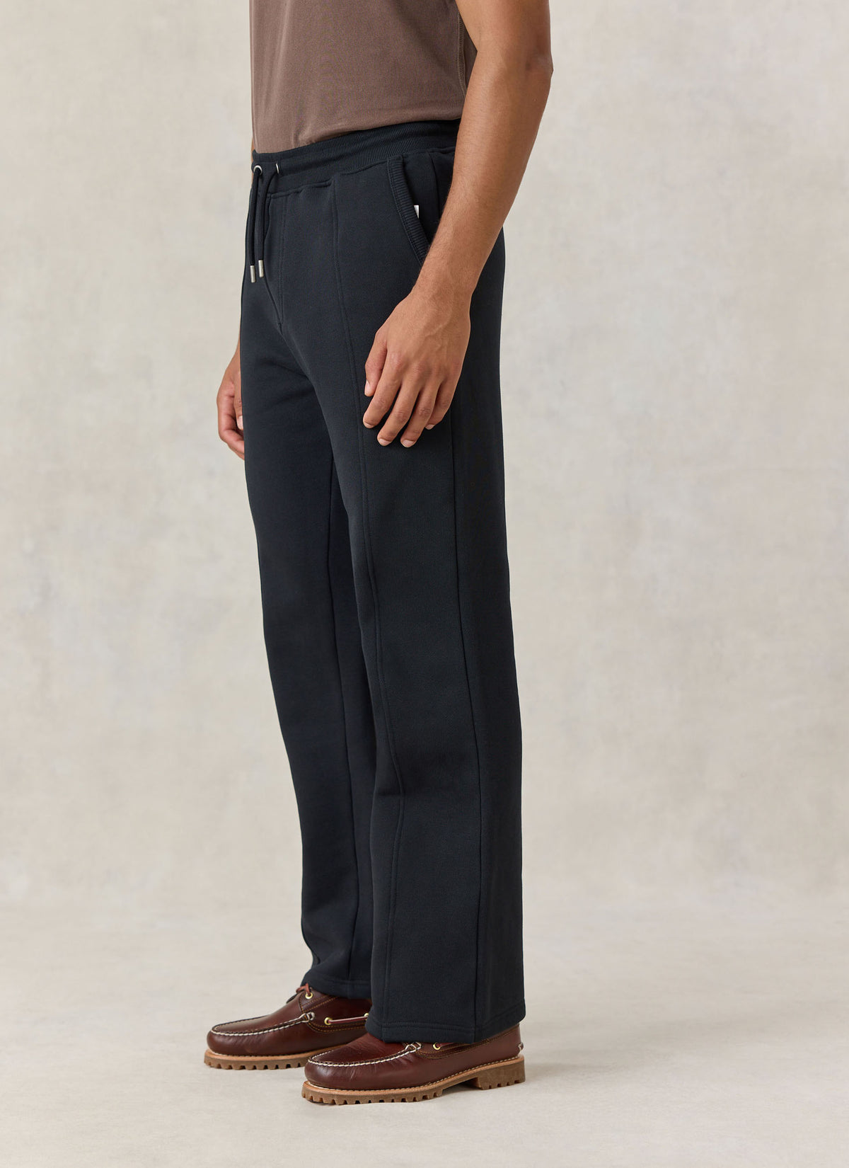 A model wearing the Percival black cotton jersey Chronicle trackpants with a straight leg and stitched front creases.