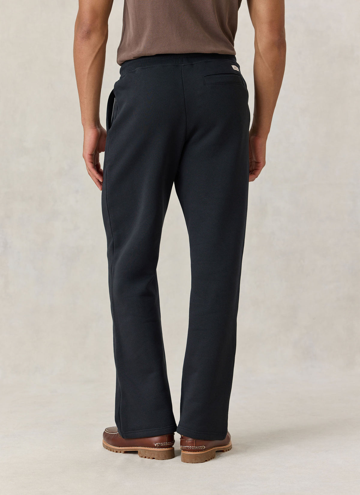 A model wearing Percival black Chronicle straight leg trackpants from the back, showing the back pocket and straight hems.