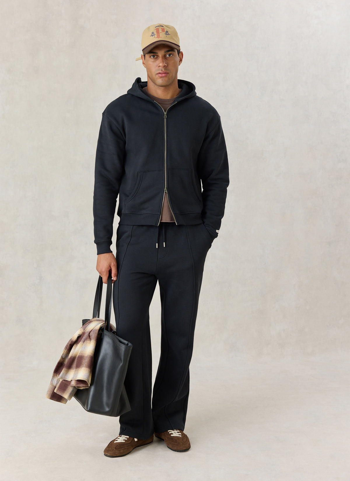 A model wearing black Percival cotton jersey trackpants and matching zip hoodie, holding a black leather tote bag.