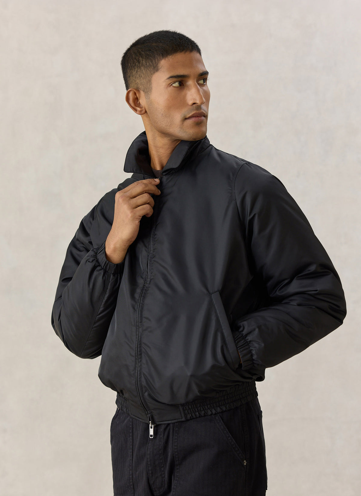 A model wearing the Percival black nylon collared bomber jacket with a two-way zip and elasticated hem.