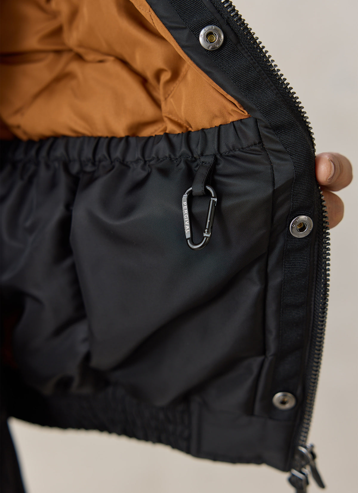 Close-up of the Percival black nylon collared bomber jacket showing the internal pocket and branded carabiner clip.