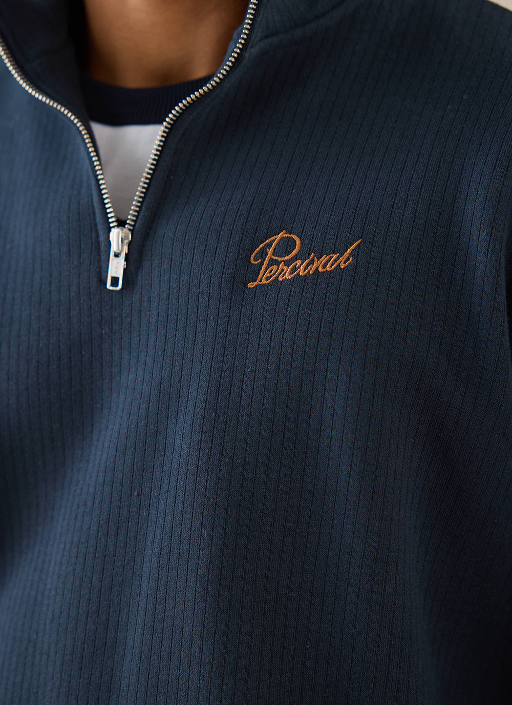 Close-up of a navy blue Percival cotton 1/4 zip jumper showing the chest branding and metal zip detail.
