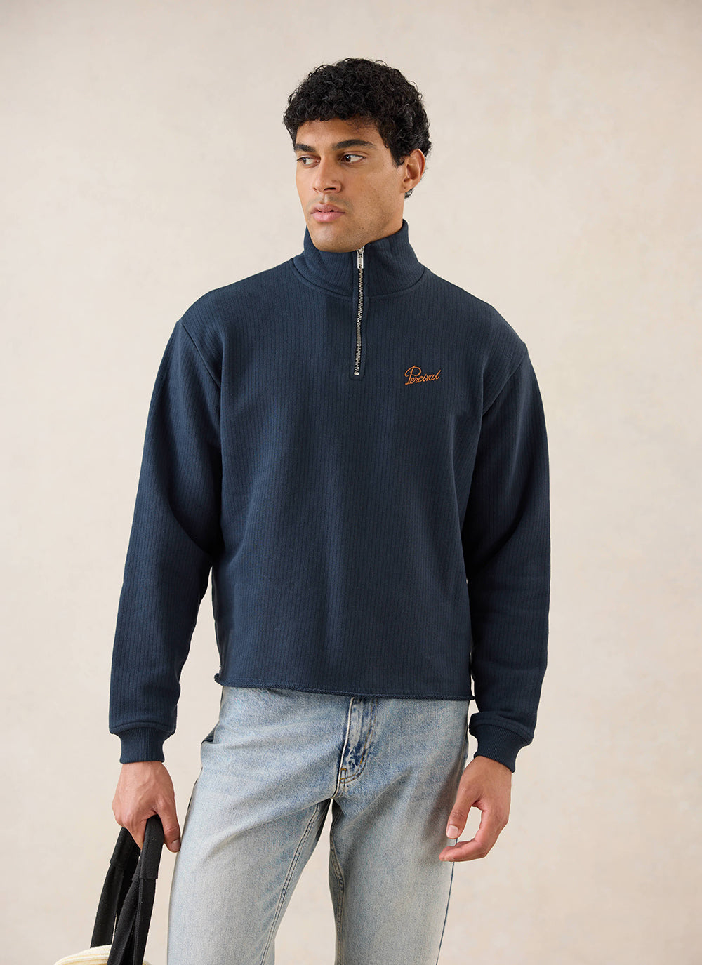 A model wearing the navy Percival Conrad funnel neck 1/4 zip jumper, styled with light blue jeans in a studio shot.