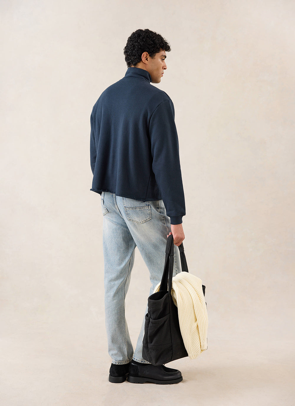 Rear view of a model wearing the navy Percival 1/4 zip jumper, styled with light wash jeans and carrying a dark tote bag.