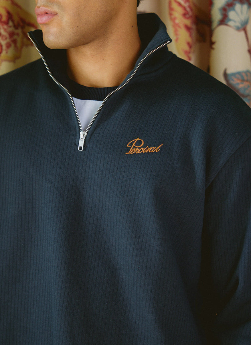Close-up of a model wearing the navy blue cotton Conrad 1/4 zip jumper with embroidered Percival logo.