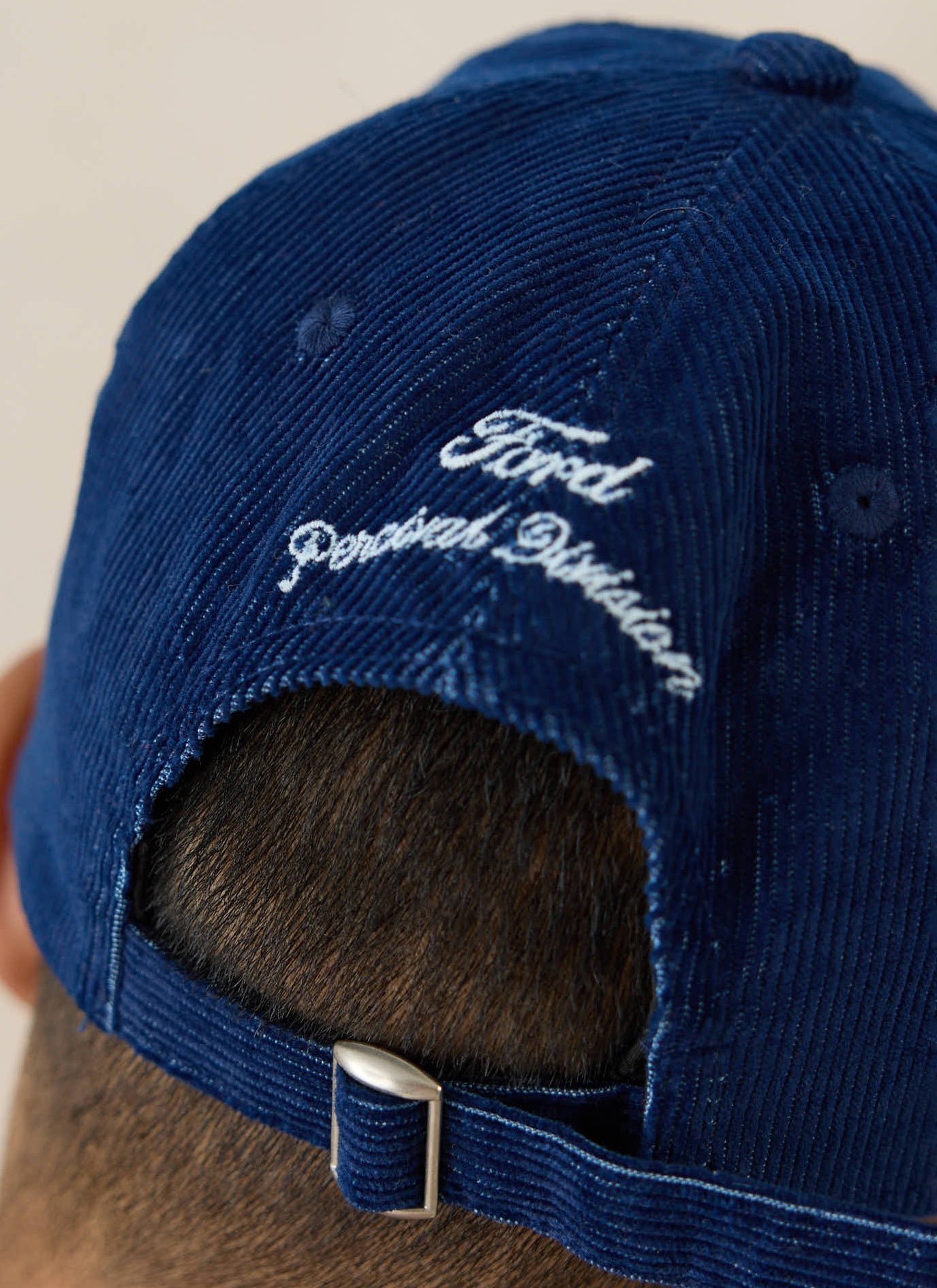 The back of the navy corduroy Ford x Percival trucker cap, showing white embroidery and an adjustable metal strap buckle.