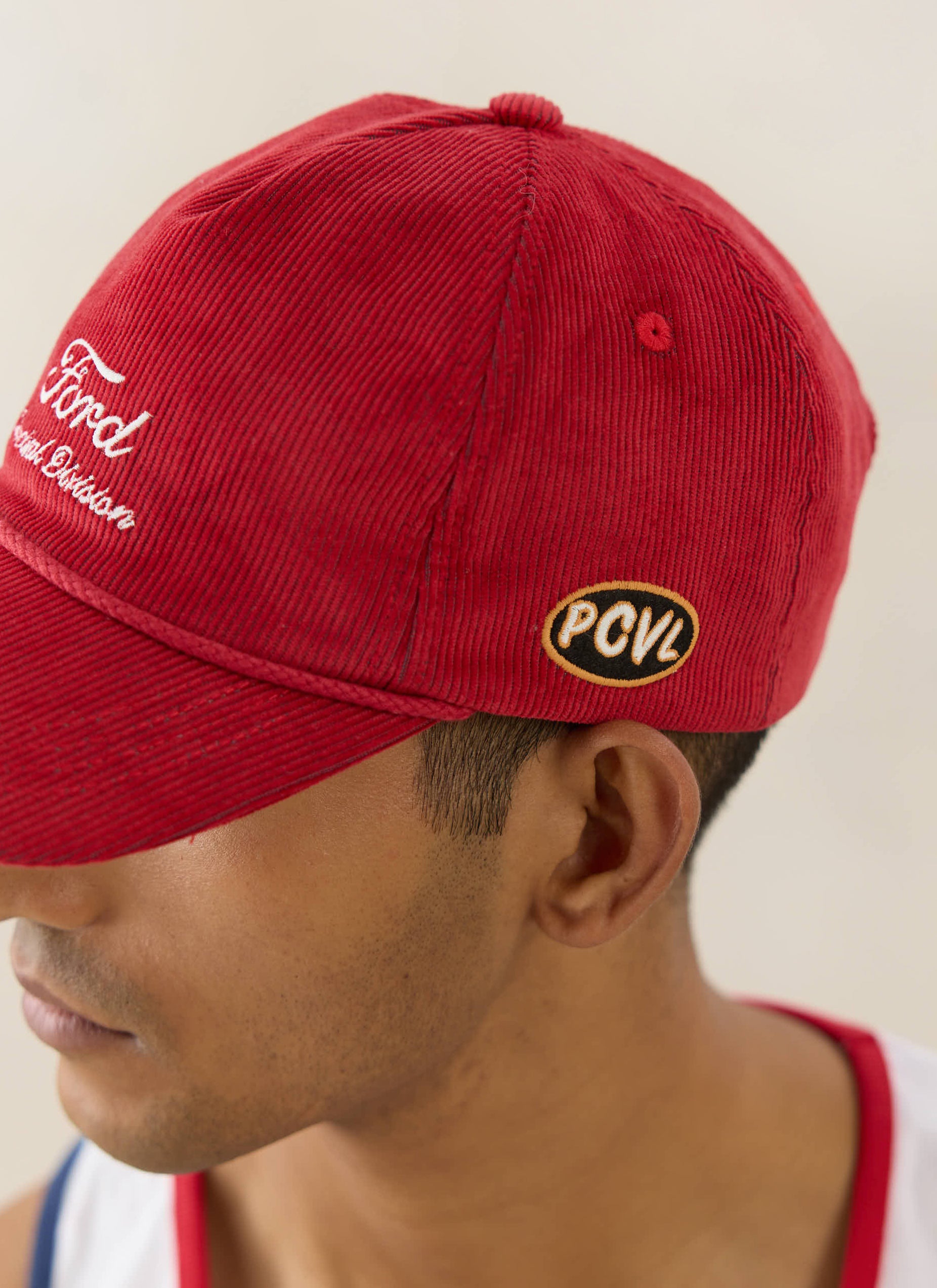 Red corduroy Ford x Percival trucker cap with white PCVL embroidery, shown in a close-up side-profile studio shot.
