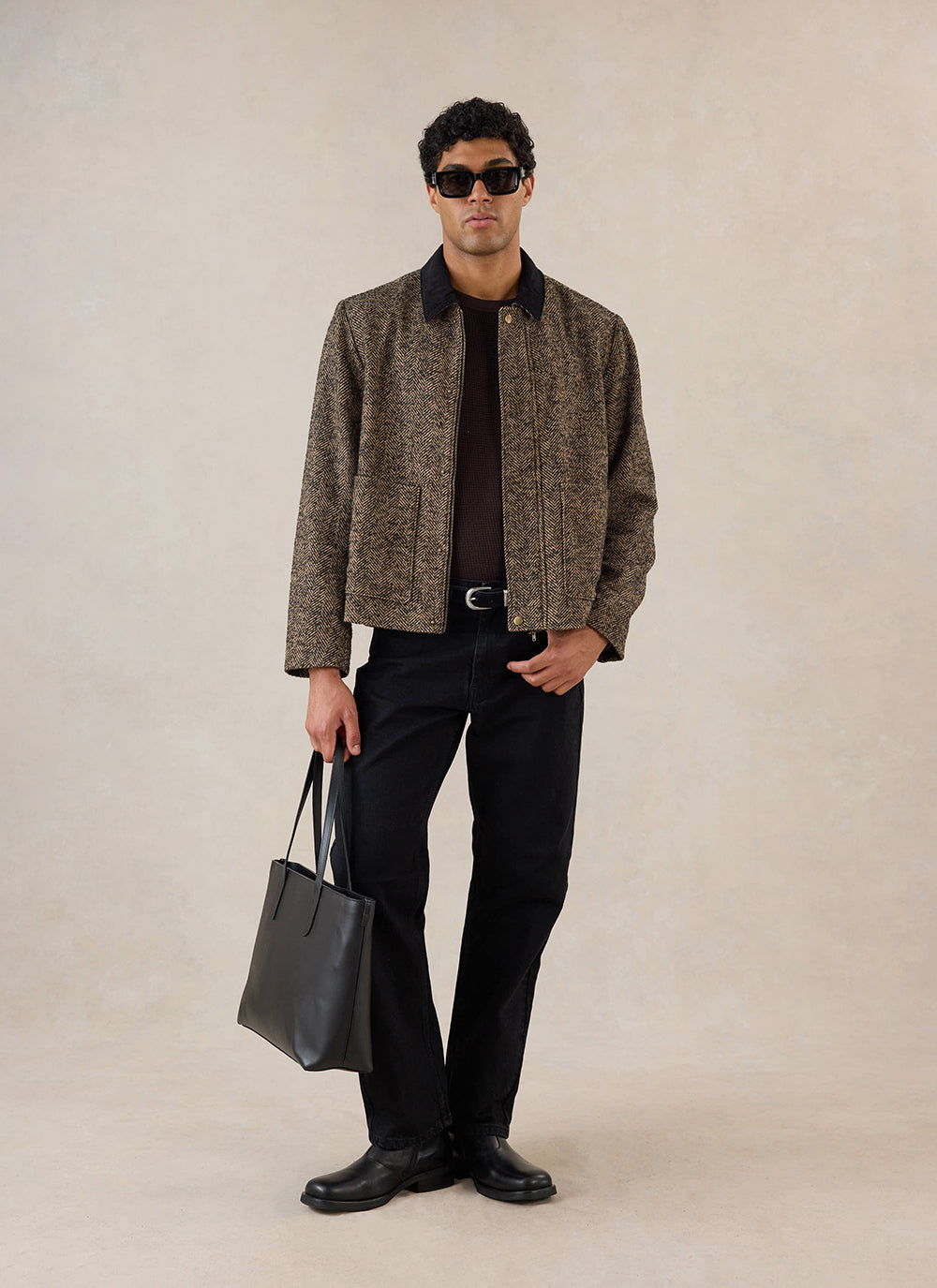 A model wears the brown Percival herringbone wool cropped jacket, styled with black trousers and a tote bag in a studio.