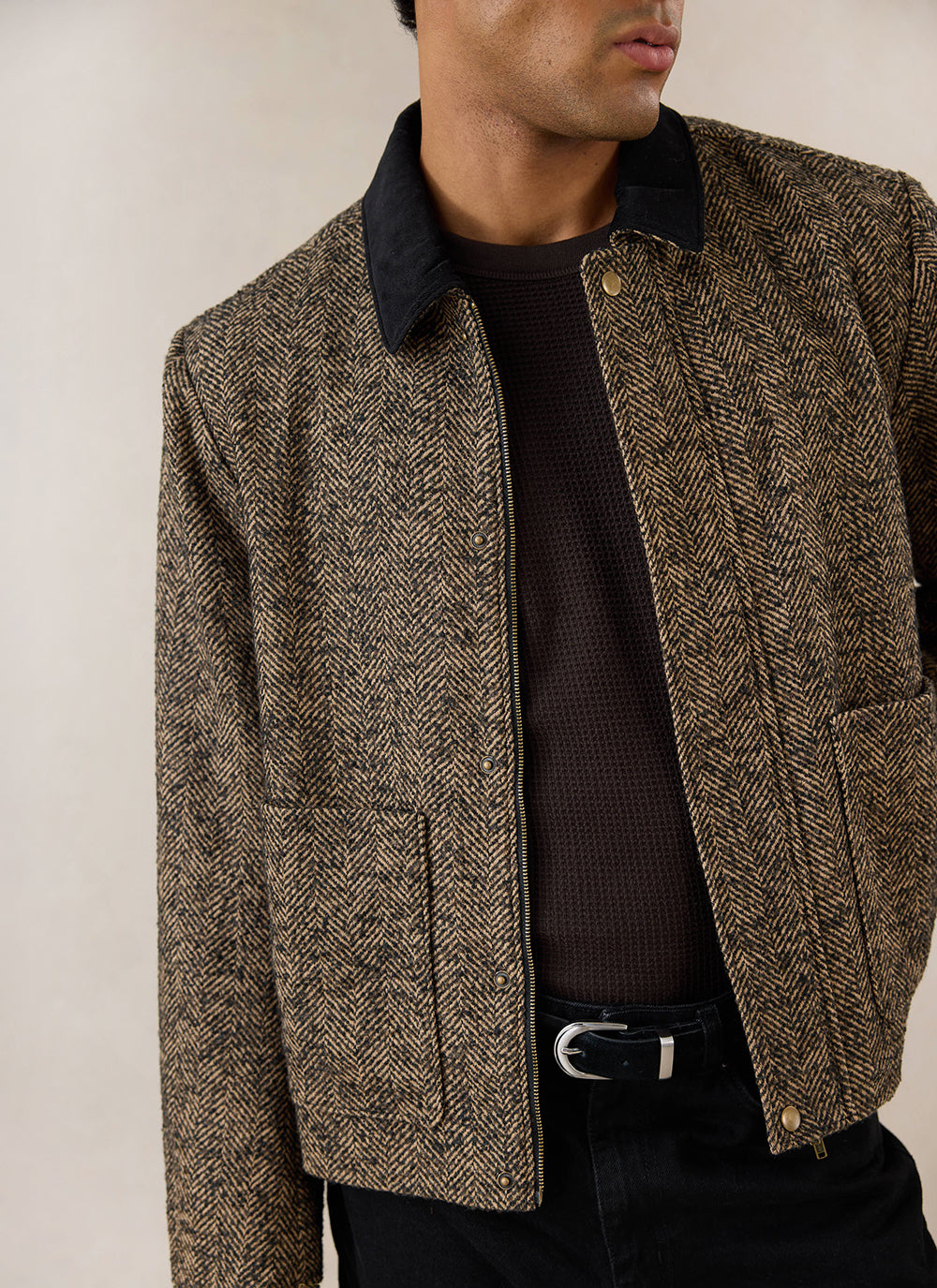 A close-up of a model wearing the brown herringbone wool boxy jacket with a contrast collar by Percival.