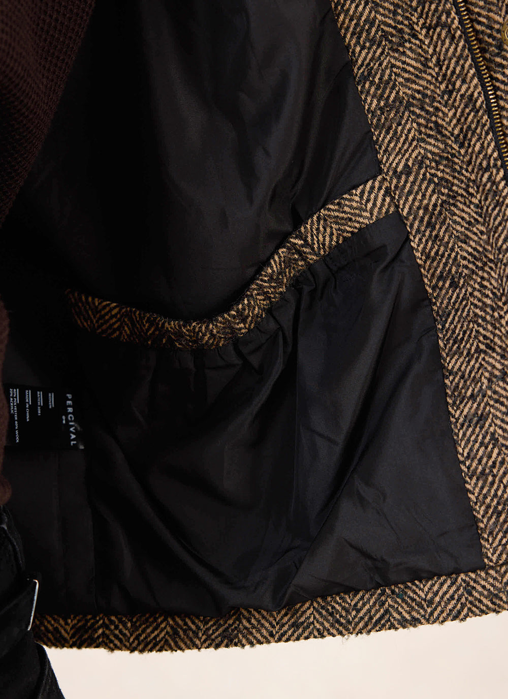 A close-up of the interior lining and pocket of the brown herringbone wool cropped boxy jacket from Percival.