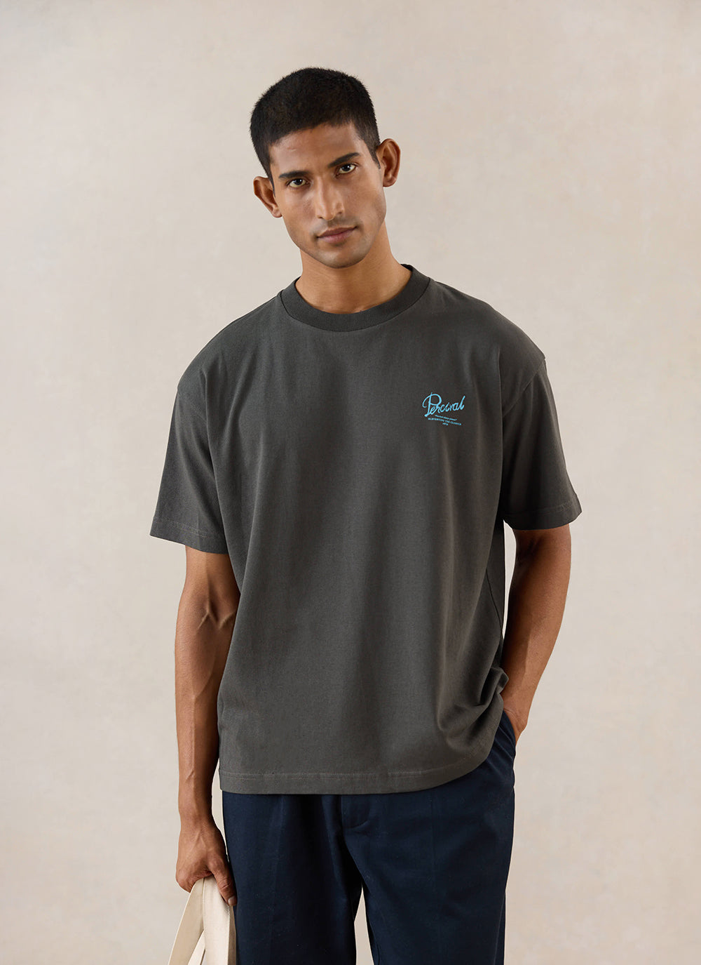 A model wears the charcoal Percival Dawson boxy t-shirt, featuring light blue embroidery on the chest.