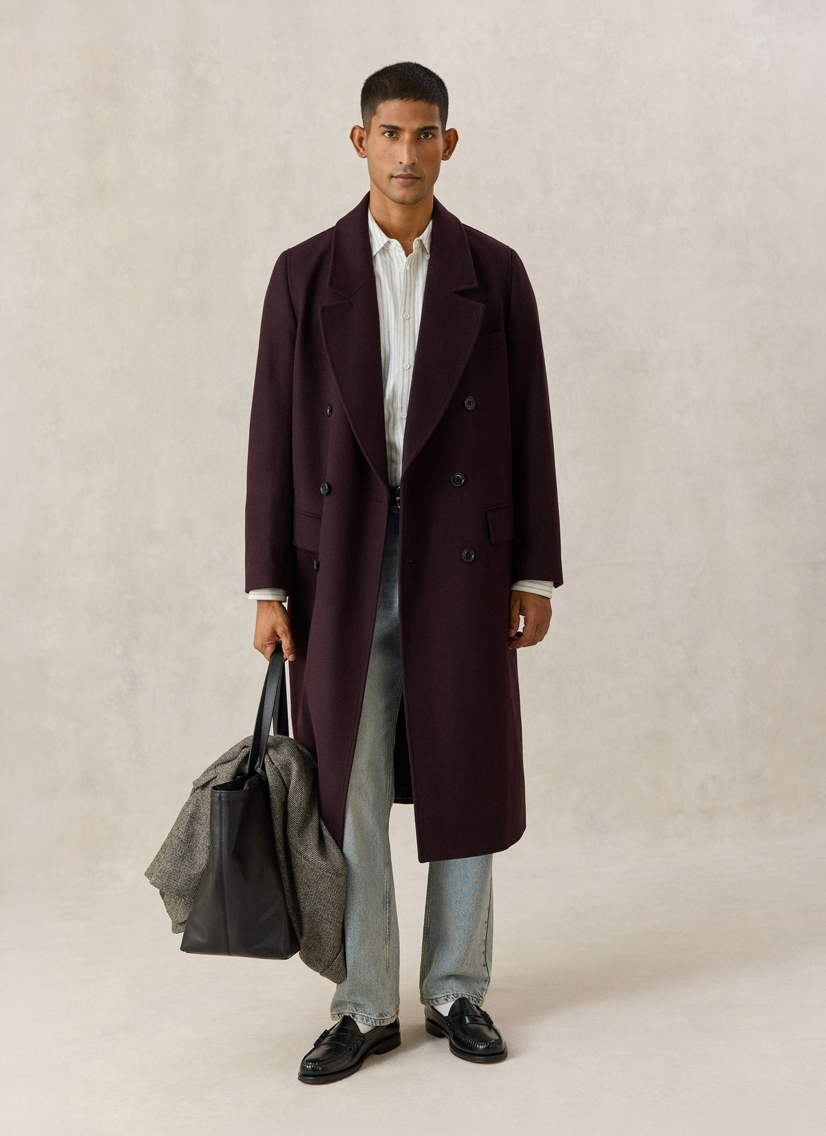 A model wearing the Percival dark brown wool-blend double-breasted overcoat, holding a black leather tote bag.