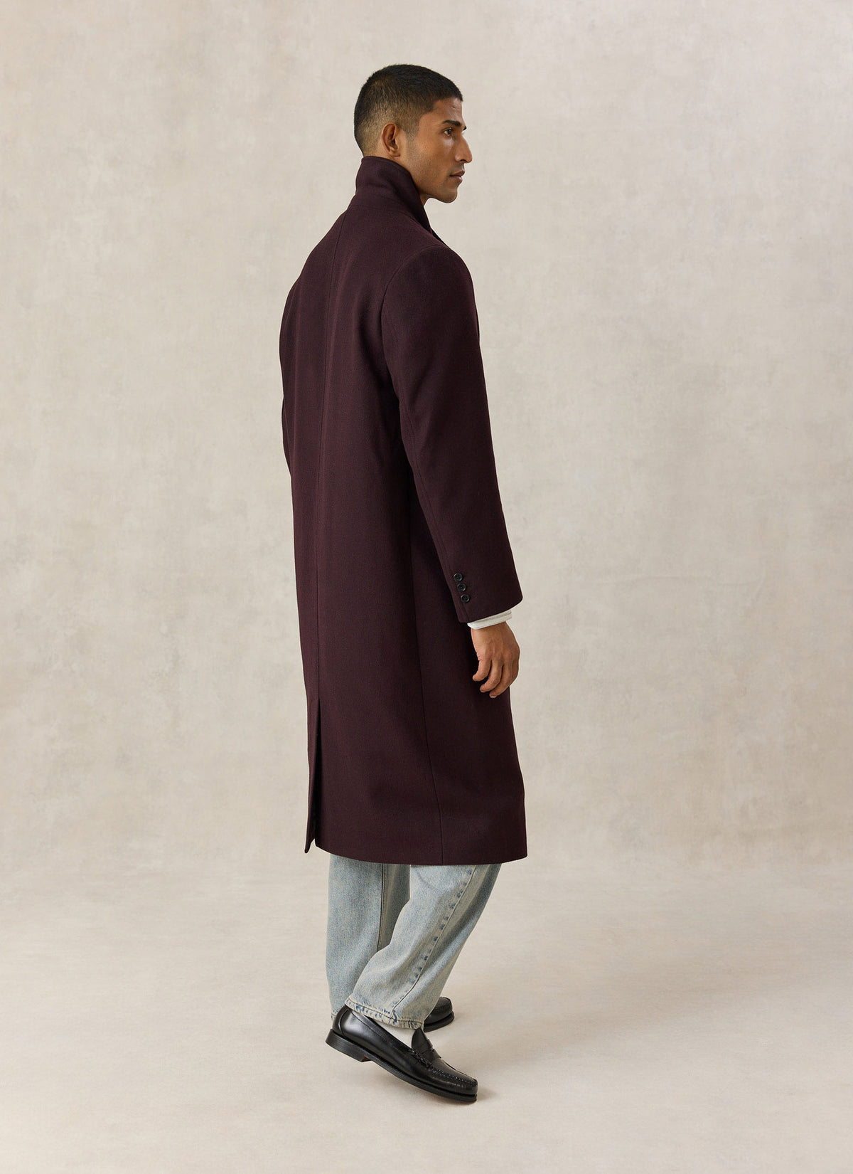 Model wearing the Percival dark brown wool blend double-breasted overcoat from the side, paired with light wash jeans.