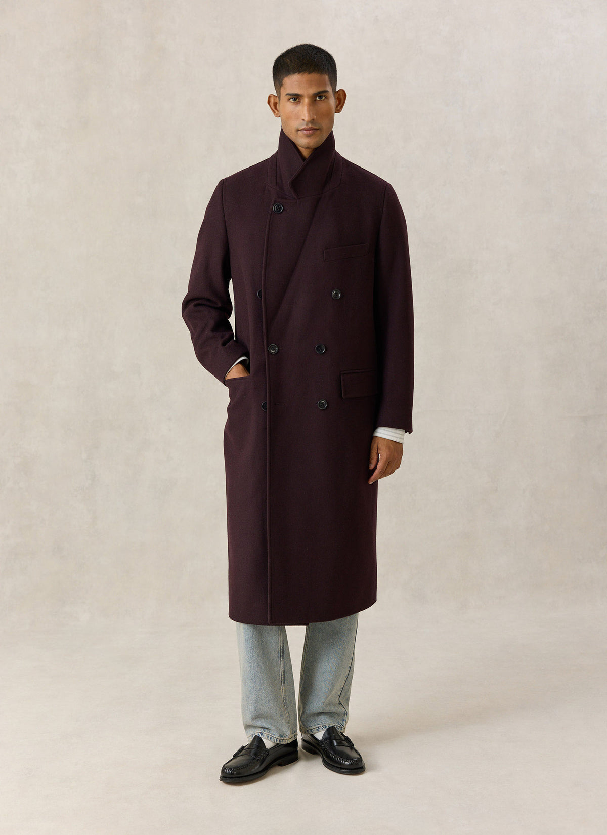A model wearing the Percival dark brown wool-blend double-breasted overcoat with a popped collar and blue jeans.