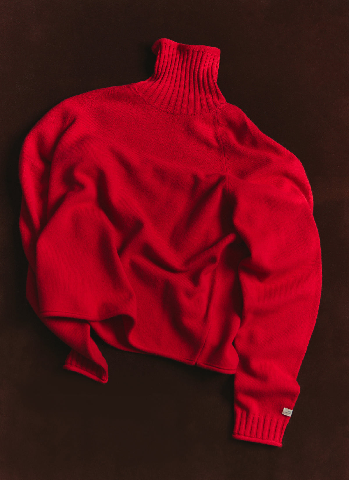 Percival red wool Dylan roll-neck jumper laid flat on a dark surface, showing raglan sleeves and ribbed cuffs.