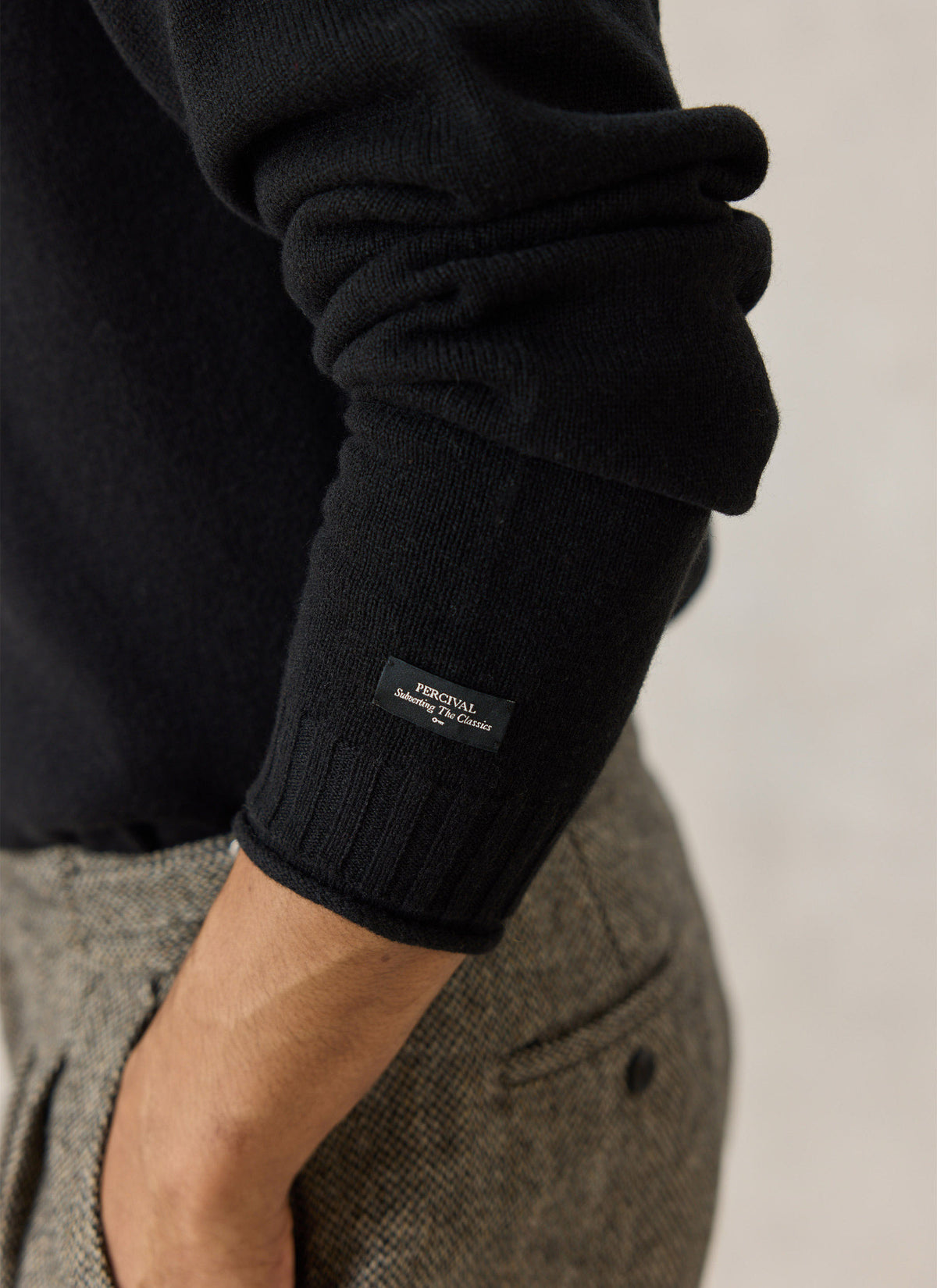 Close-up of the black Percival Dylan wool jumper sleeve, showing the ribbed cuff and branded woven label.