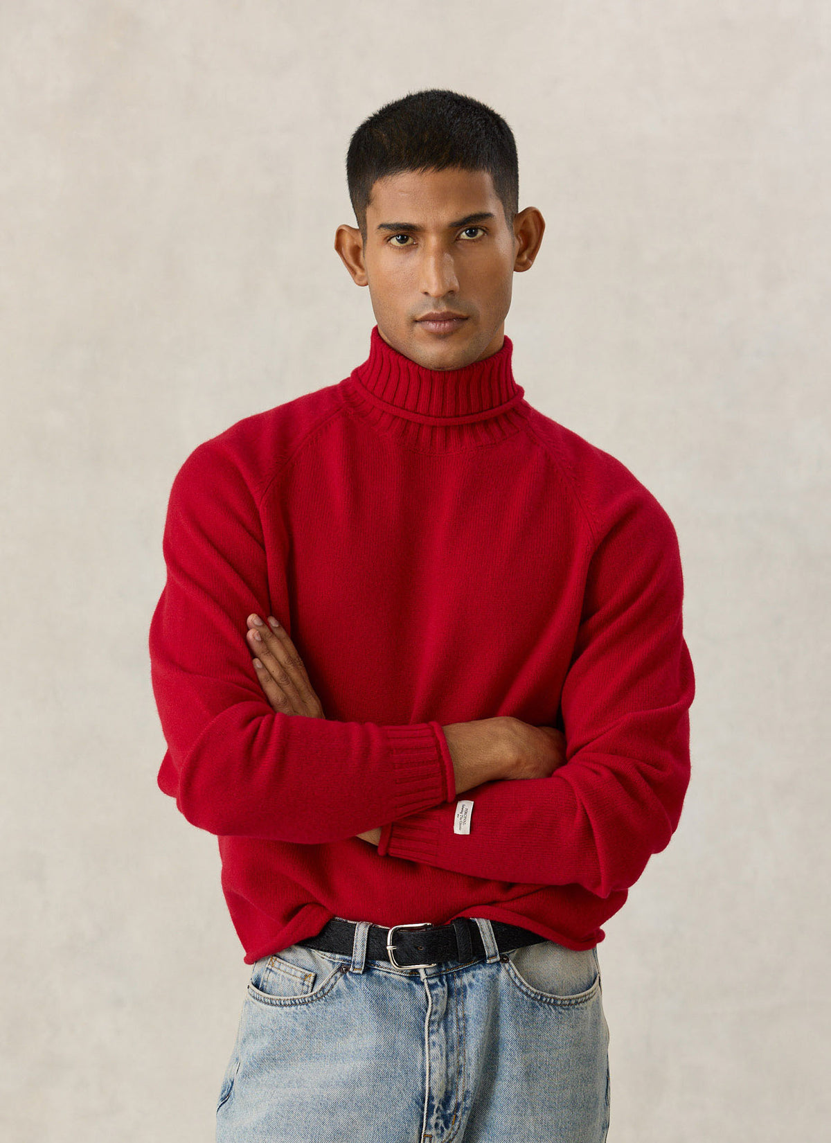 A model wearing the Percival red Dylan roll-neck jumper in 100% wool with raglan sleeves, paired with jeans.