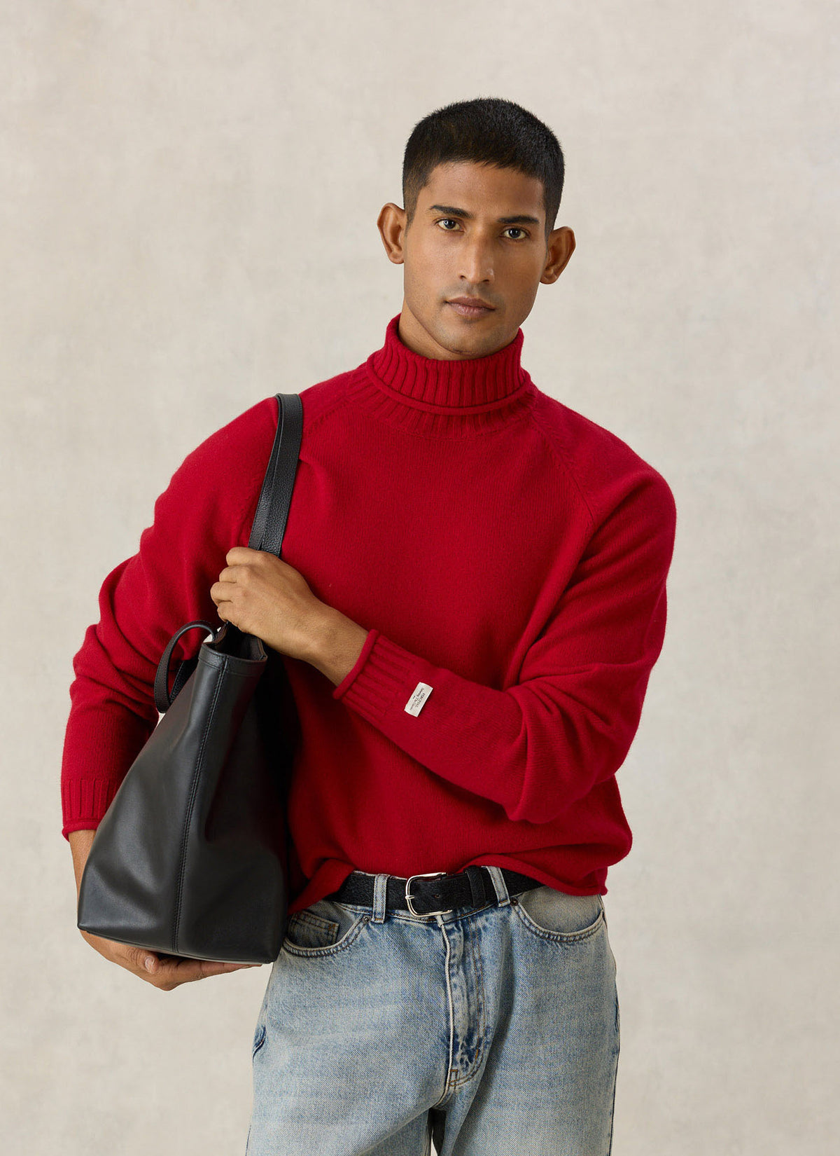A model wearing the Percival red wool roll-neck jumper with raglan sleeves, holding a black leather tote bag.