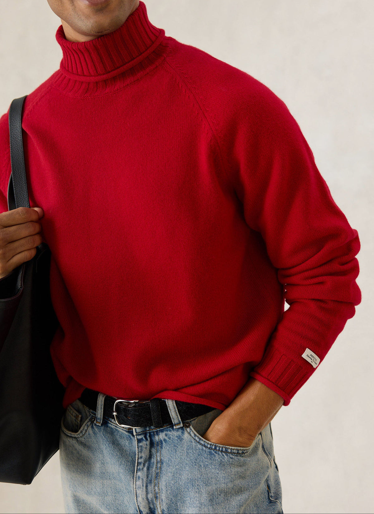 A model wearing the Percival red wool Dylan roll-neck jumper with jeans and a black bag.