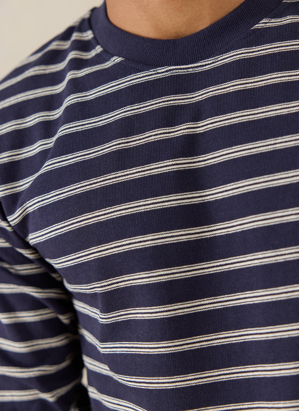 A close-up of a model wearing the navy stripe Arlo Breton T-shirt from Percival, highlighting the ribbed crew neck.