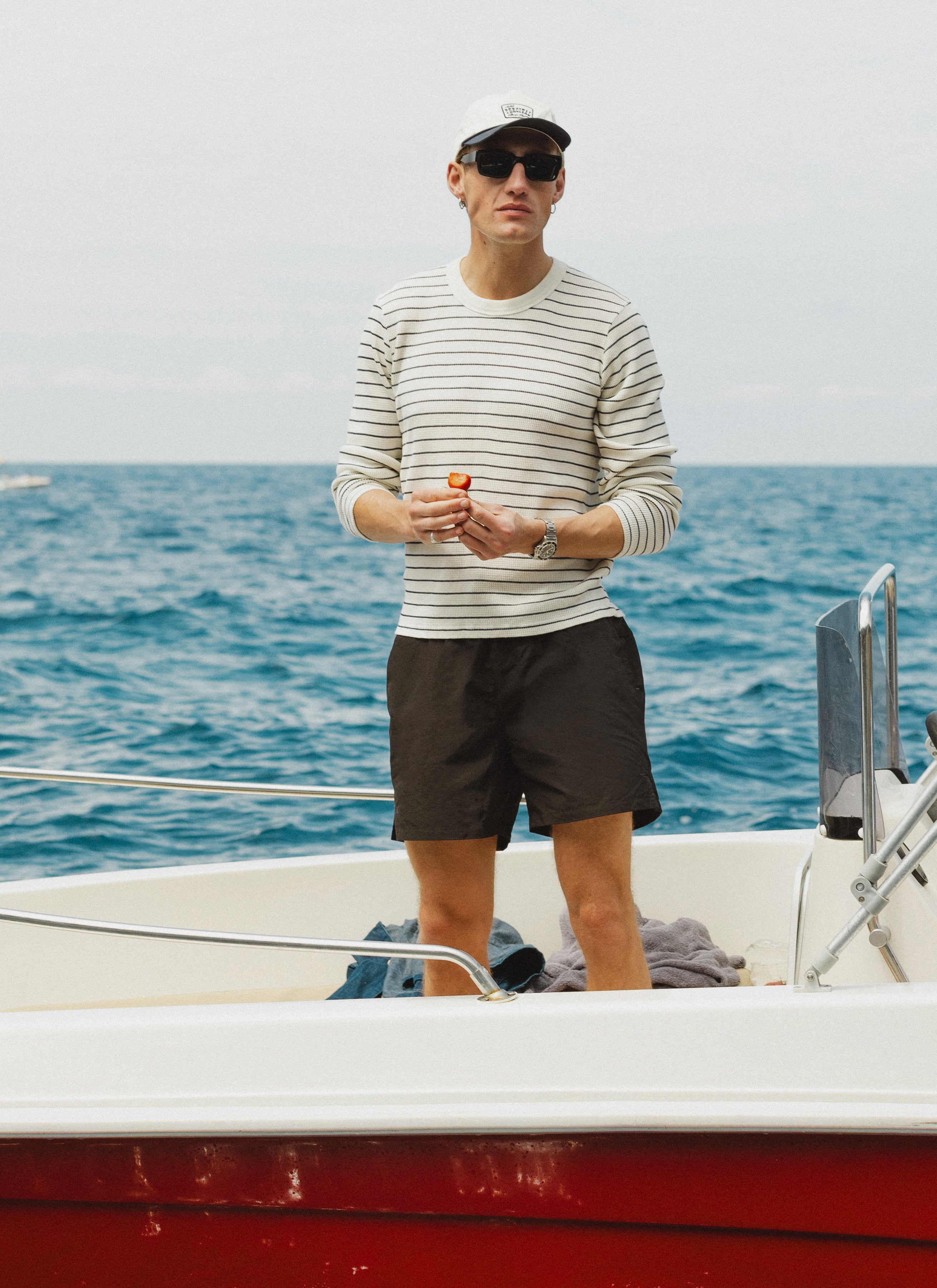 A model wears the cream stripe Percival Ernie Waffle Long Sleeve T Shirt while standing on a boat on the sea.