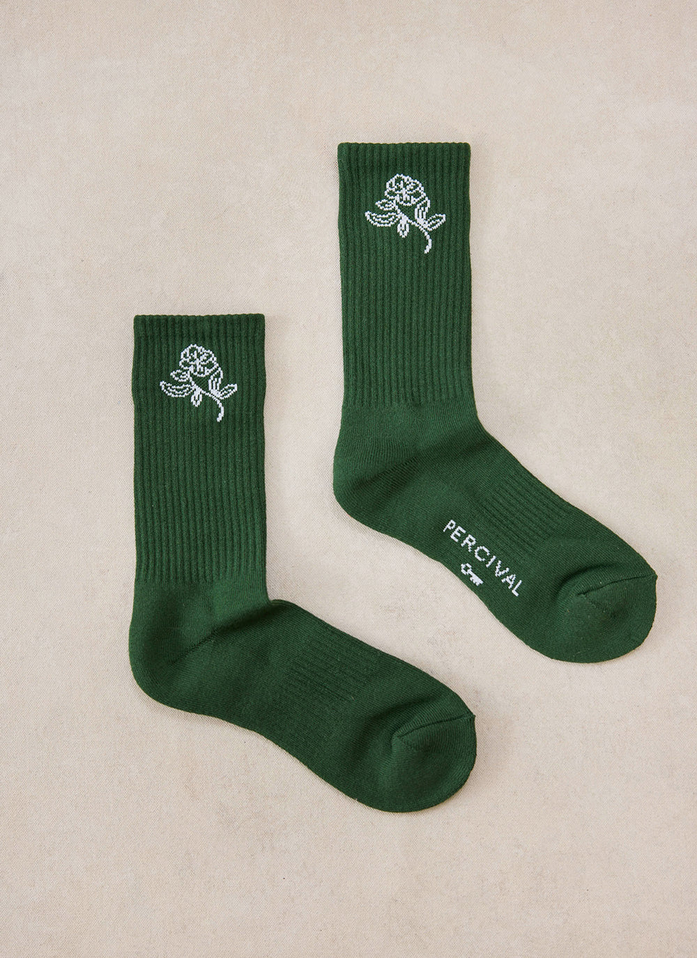 A flat lay of the forest green Earl Jacquard cotton socks featuring a white floral motif and Percival branding.