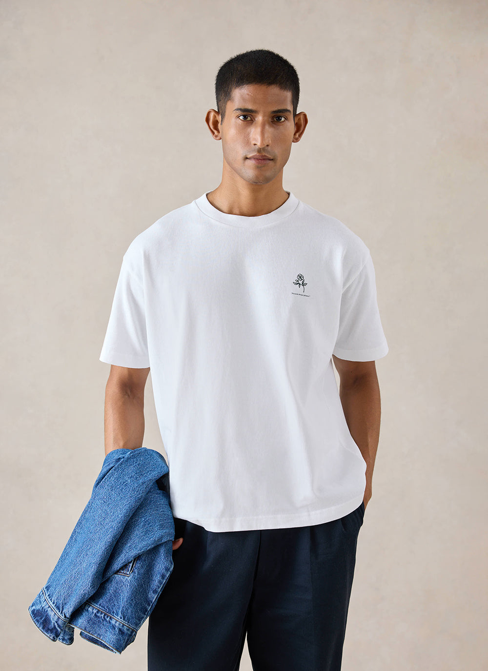 A model wears the white Percival Earl oversized t-shirt, featuring a small chest graphic, holding a blue jacket.