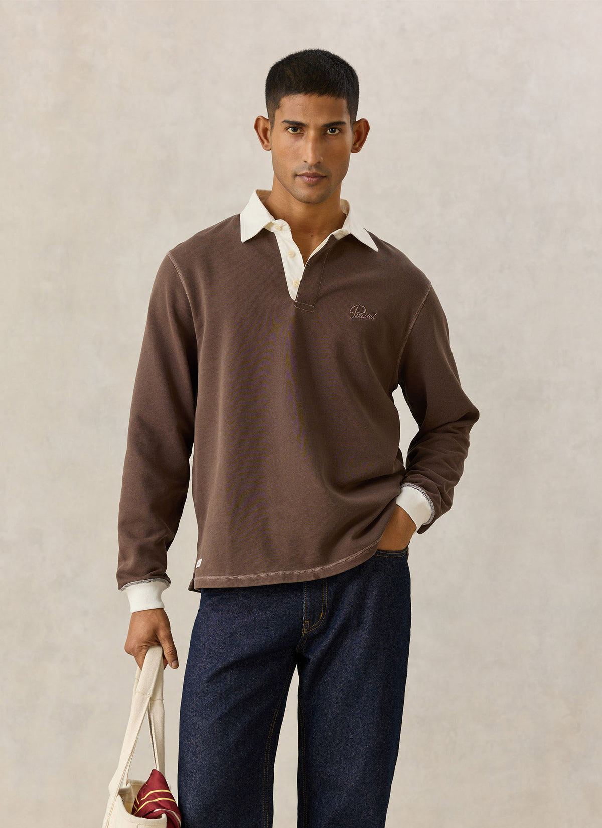 A model wearing the Percival brown cotton twill rugby polo shirt with a contrasting cream collar and cuffs.