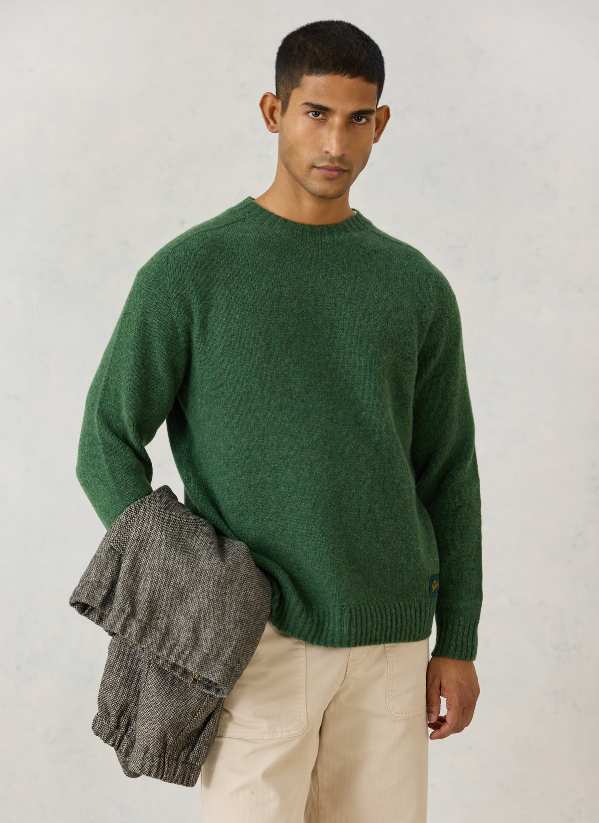 A model wearing the Percival forest green lambswool crew neck jumper, holding a patterned coat.