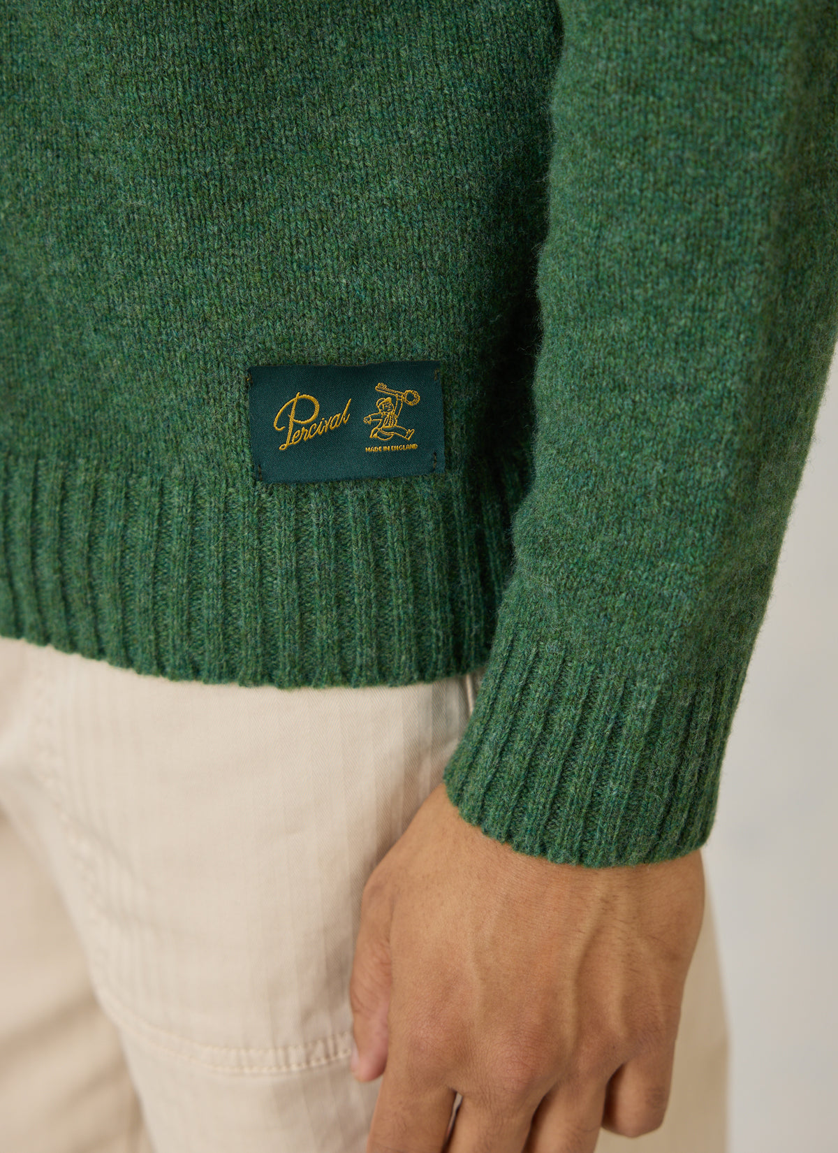 A close-up of the forest green Percival lambswool jumper, highlighting the ribbed hem and the Made in England brand label.