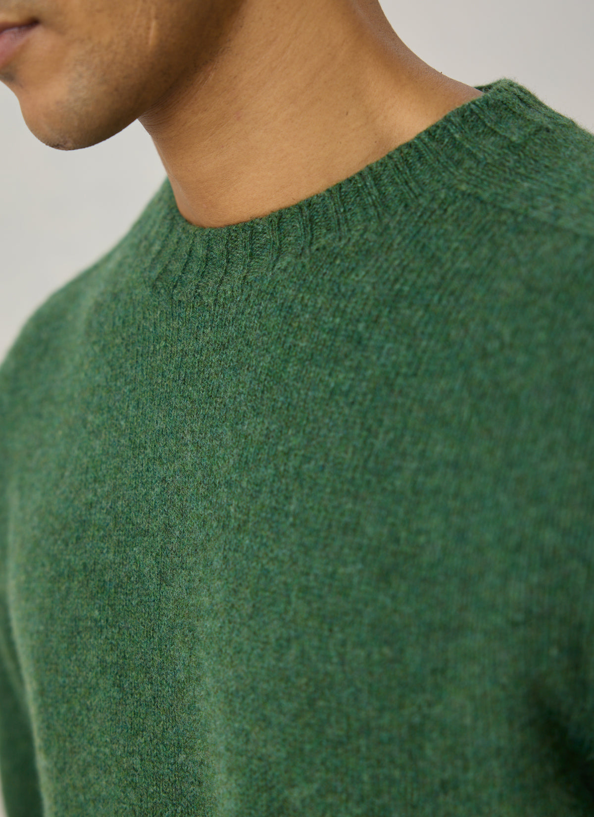 A close-up of the Percival forest green lambswool jumper showing the ribbed crew neck and textured 6-ply yarn.