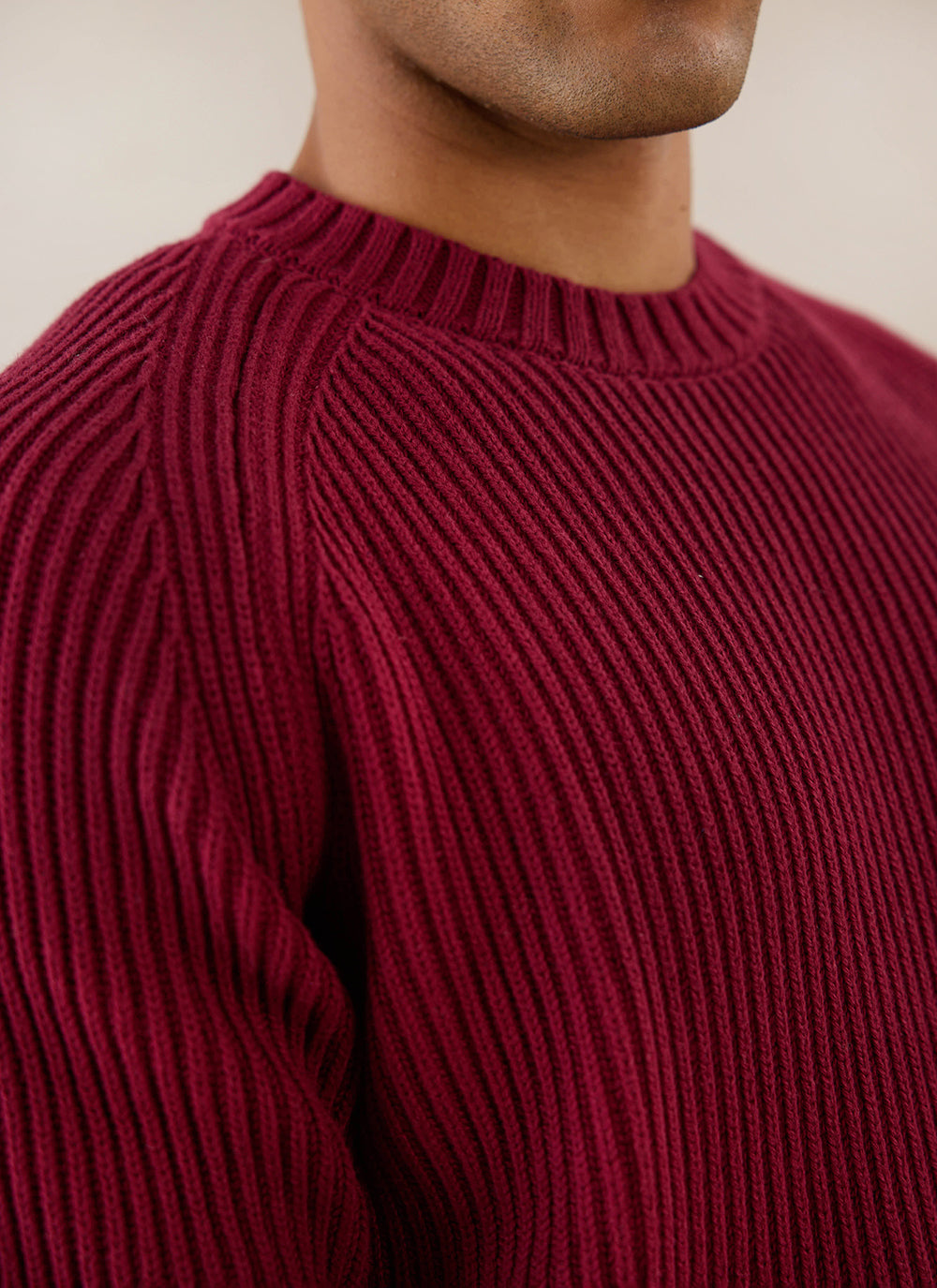 A close-up of a model wearing the burgundy Fisherman knitted jumper from Percival, highlighting the heavy cotton rib texture.