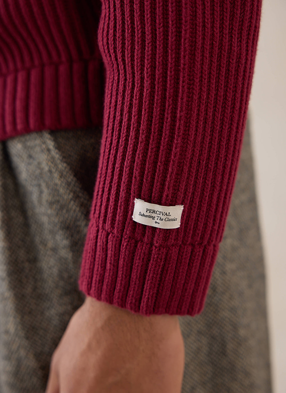 Close-up of the brand label on the sleeve of the burgundy Fisherman knitted jumper from Percival.