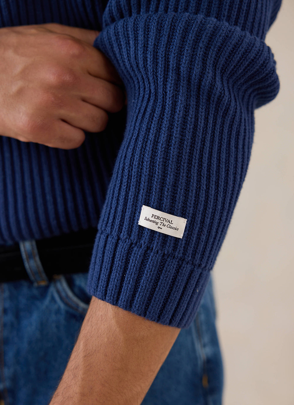 Close-up of a model wearing the navy Percival Fisherman Knitted Jumper, highlighting the textured ribbing and branding label.