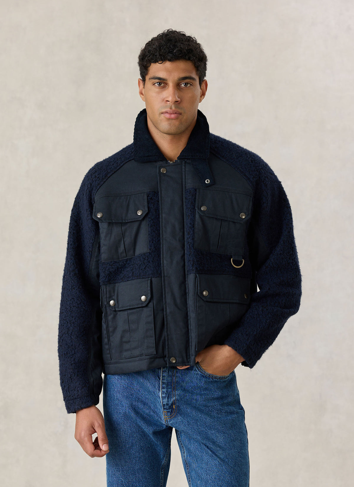 A model wearing the Percival navy blue Fletcher utility fleece and wax jacket with four flap pockets and jeans.