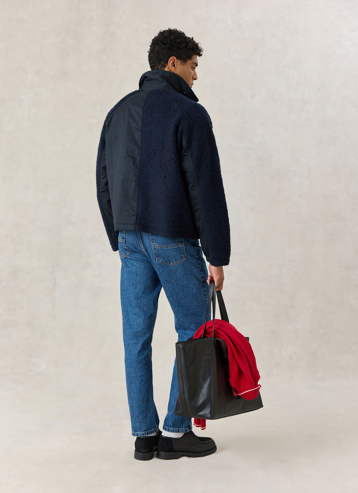 A model from the back wearing the Percival navy Fletcher utility jacket and blue jeans, holding a black tote bag.