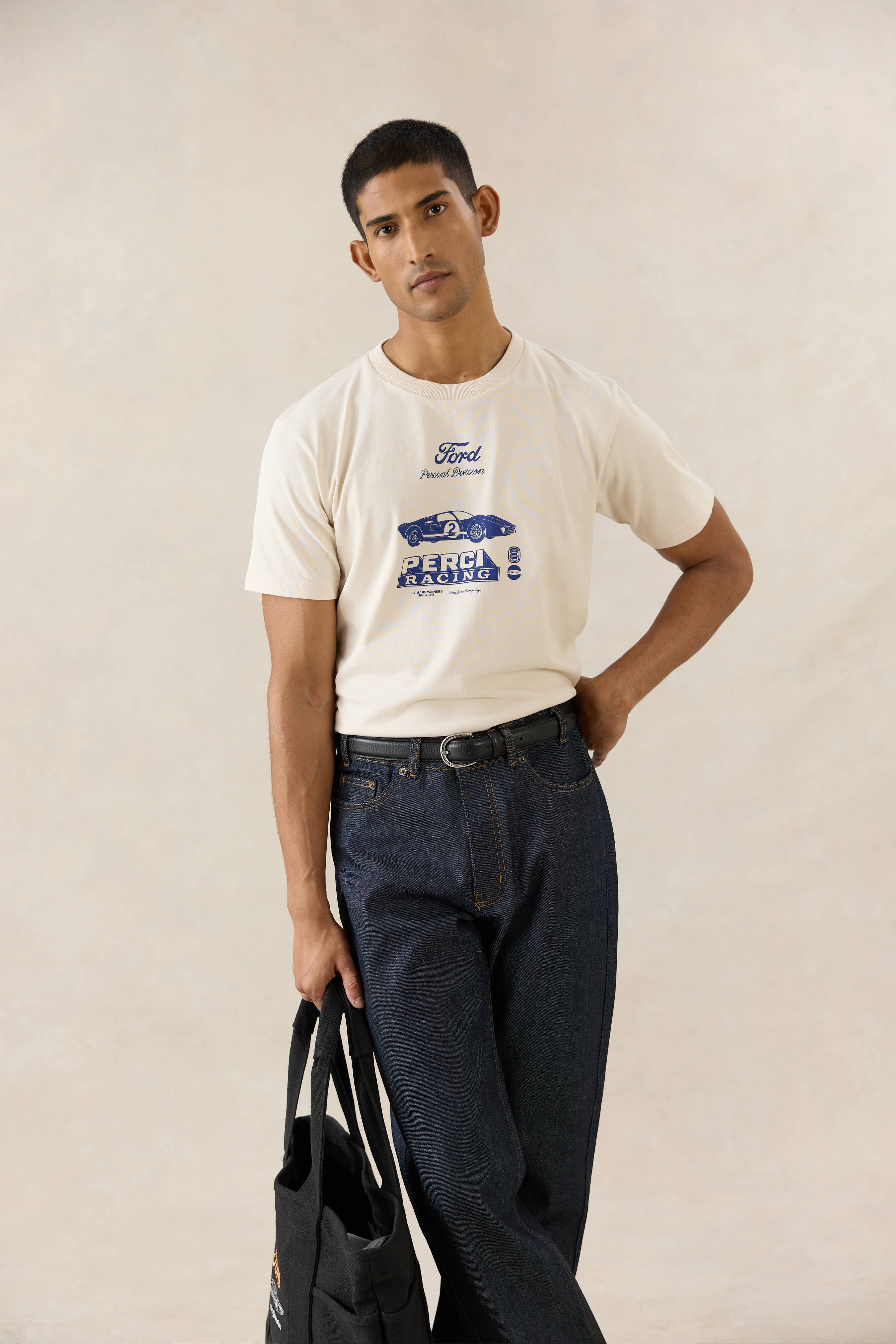 A model wears the cream Ford x Percival GT40 Archive T-shirt, styled with dark Percival straight leg heritage denim jeans.