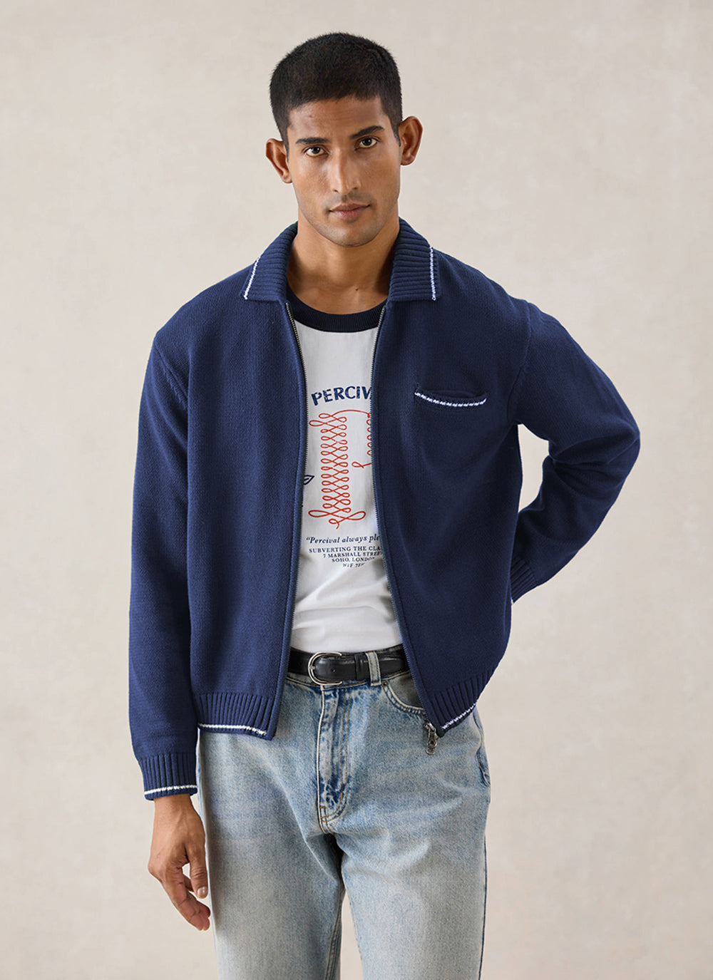 A model wearing the navy Percival zip-up cotton knit cardigan over a graphic t-shirt and jeans.
