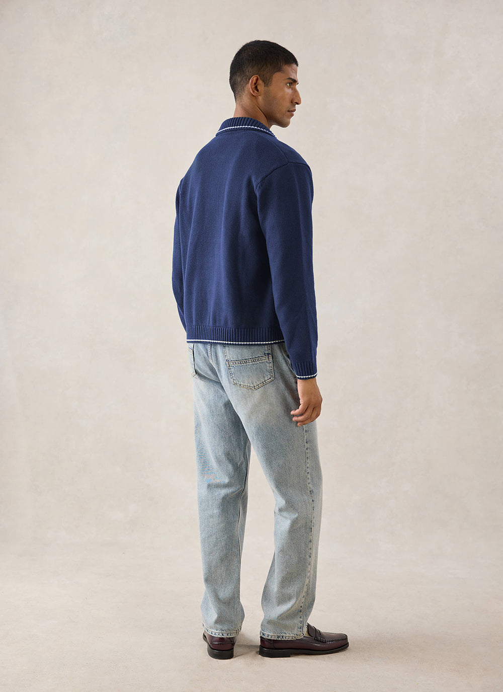 A model wearing the navy Percival Gardner dense knitted zip cardigan from behind, styled with light blue jeans.