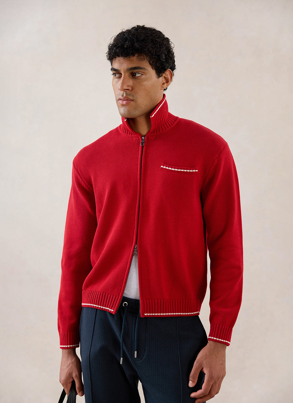 A model wearing a red Percival knitted zip-up cardigan with white contrast stitching detail.