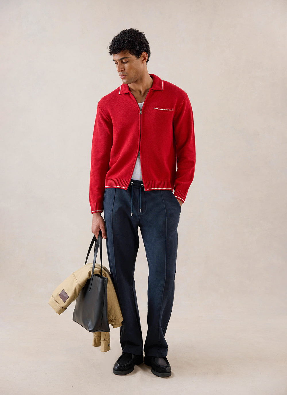 A model wearing the red Percival Gardner zip cardigan in cotton with navy trousers, holding a black tote bag.