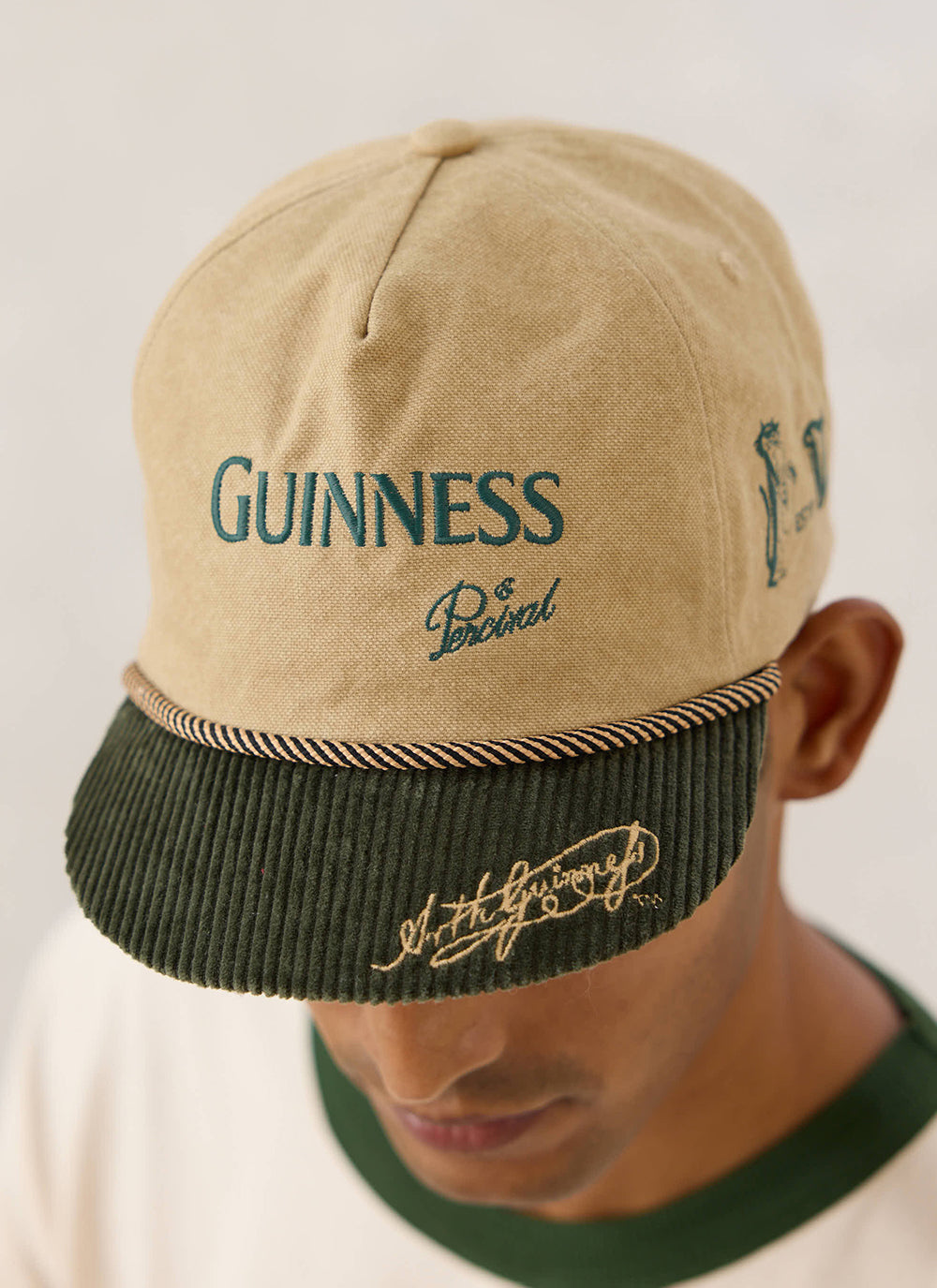 Close-up of the beige Guinness x Percival short peak cap featuring green corduroy brim and front embroidery.