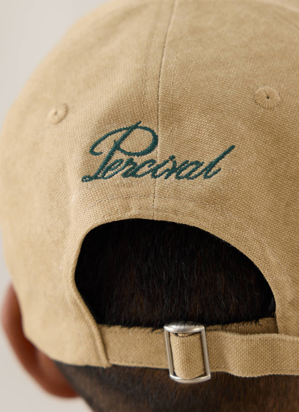 Close-up of the back of the beige Guinness x Percival cotton cap, showing green embroidery and the adjustable metal strap.