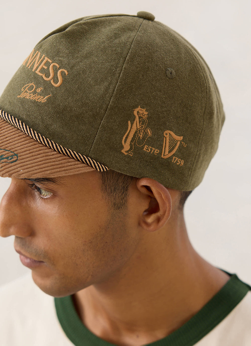 Side profile of a model wearing the Guinness x Percival forest green cap, showing the embroidered branding and cord peak.