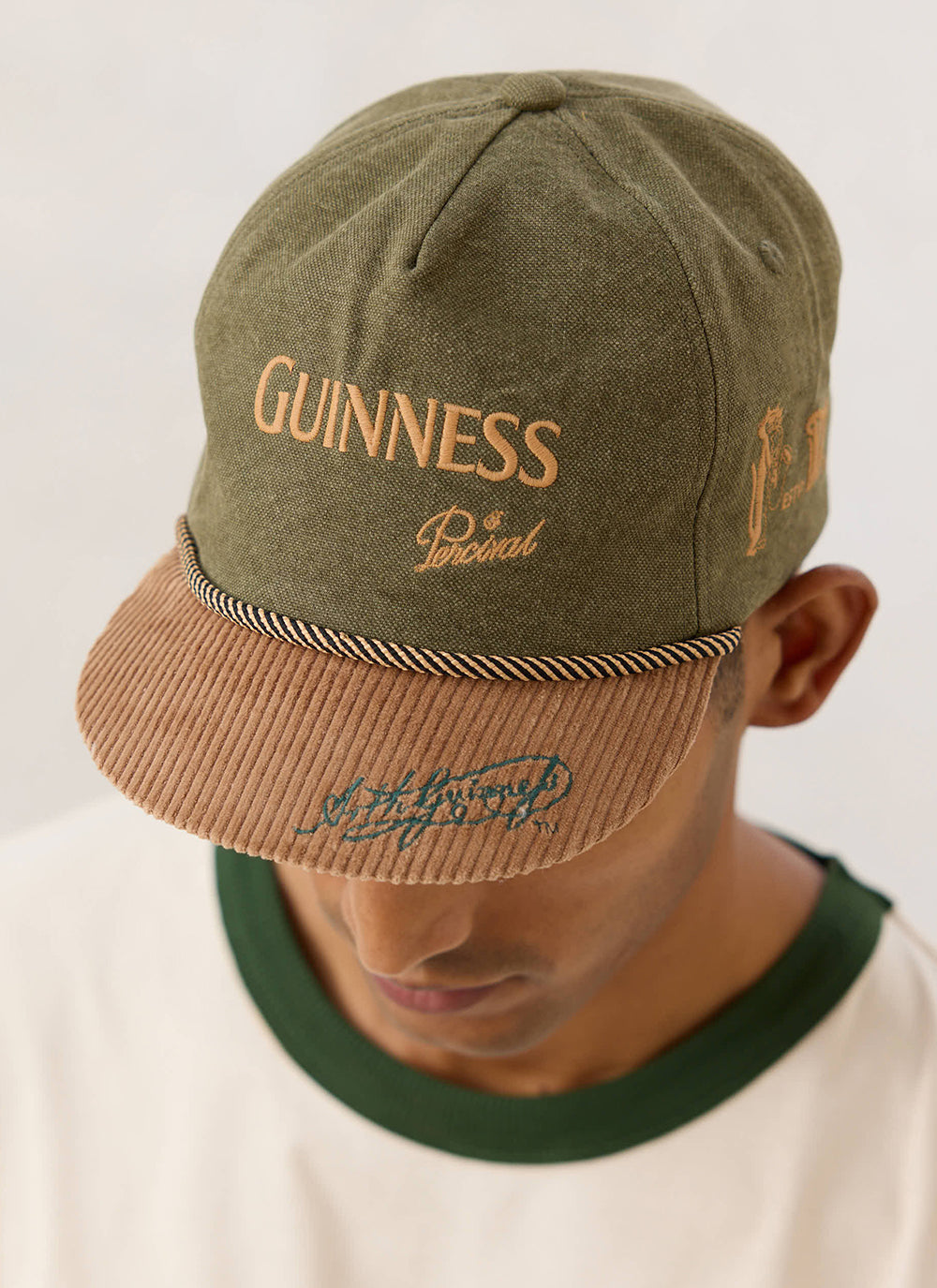 Close-up of the Guinness x Percival forest green cap with a brown corduroy peak, rope trim, and embroidered branding.