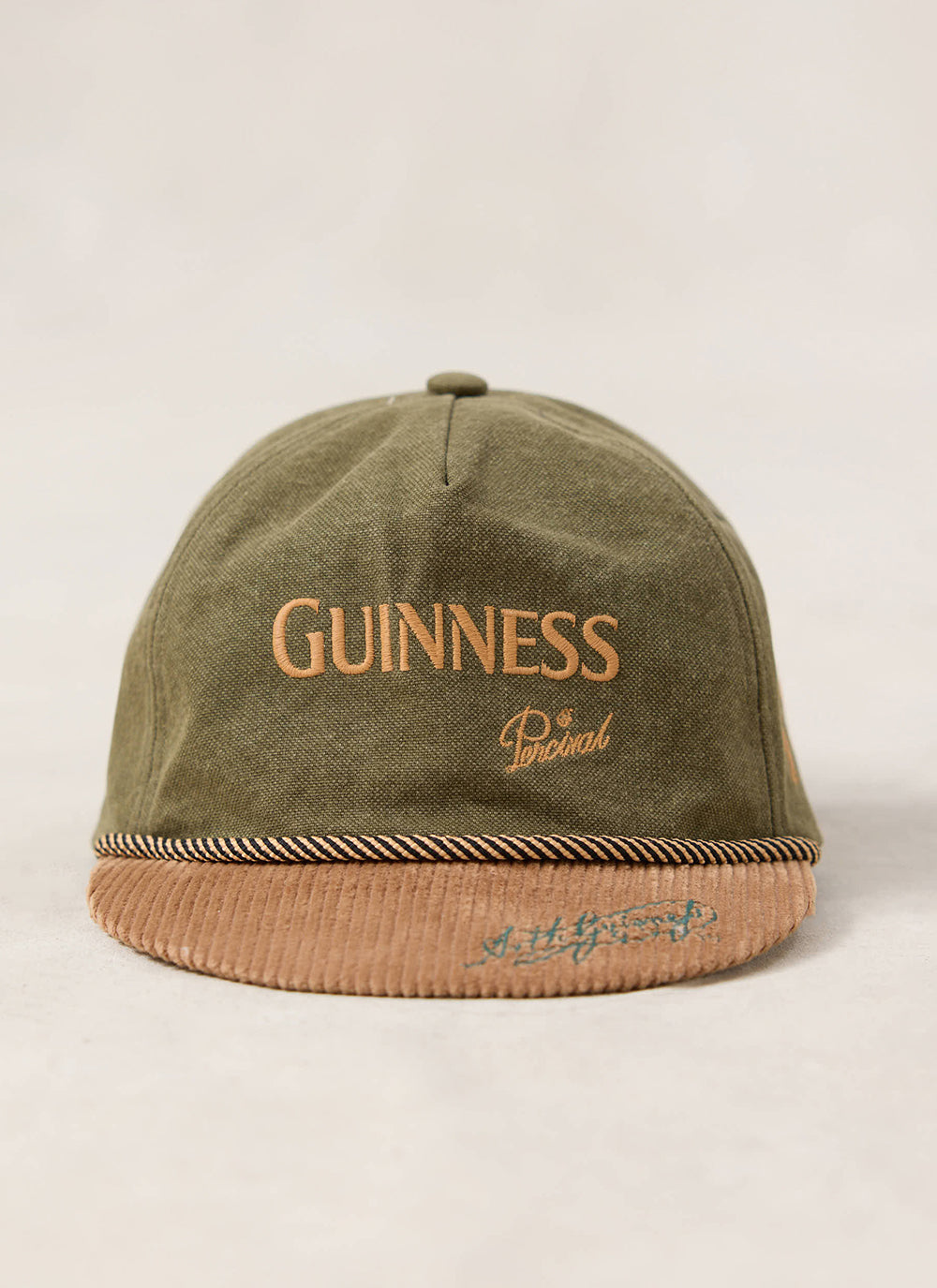 Front view of the Guinness x Percival forest green cotton short peak cap with contrast cord peak and embroidered branding.