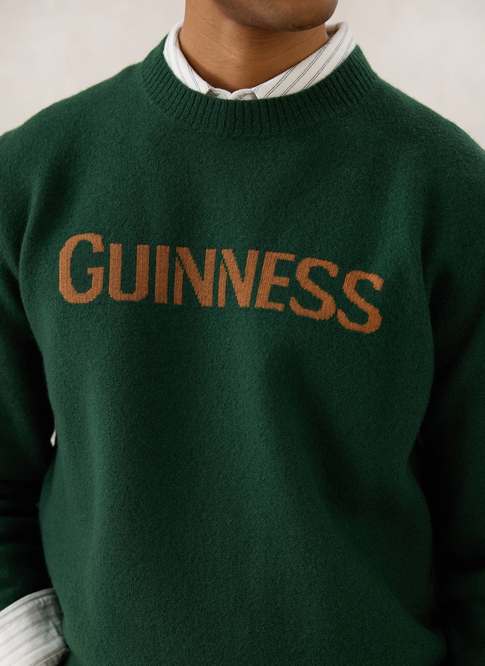 A close-up of the Guinness x Percival forest green merino wool jumper showing the bold jacquard branding on the chest.