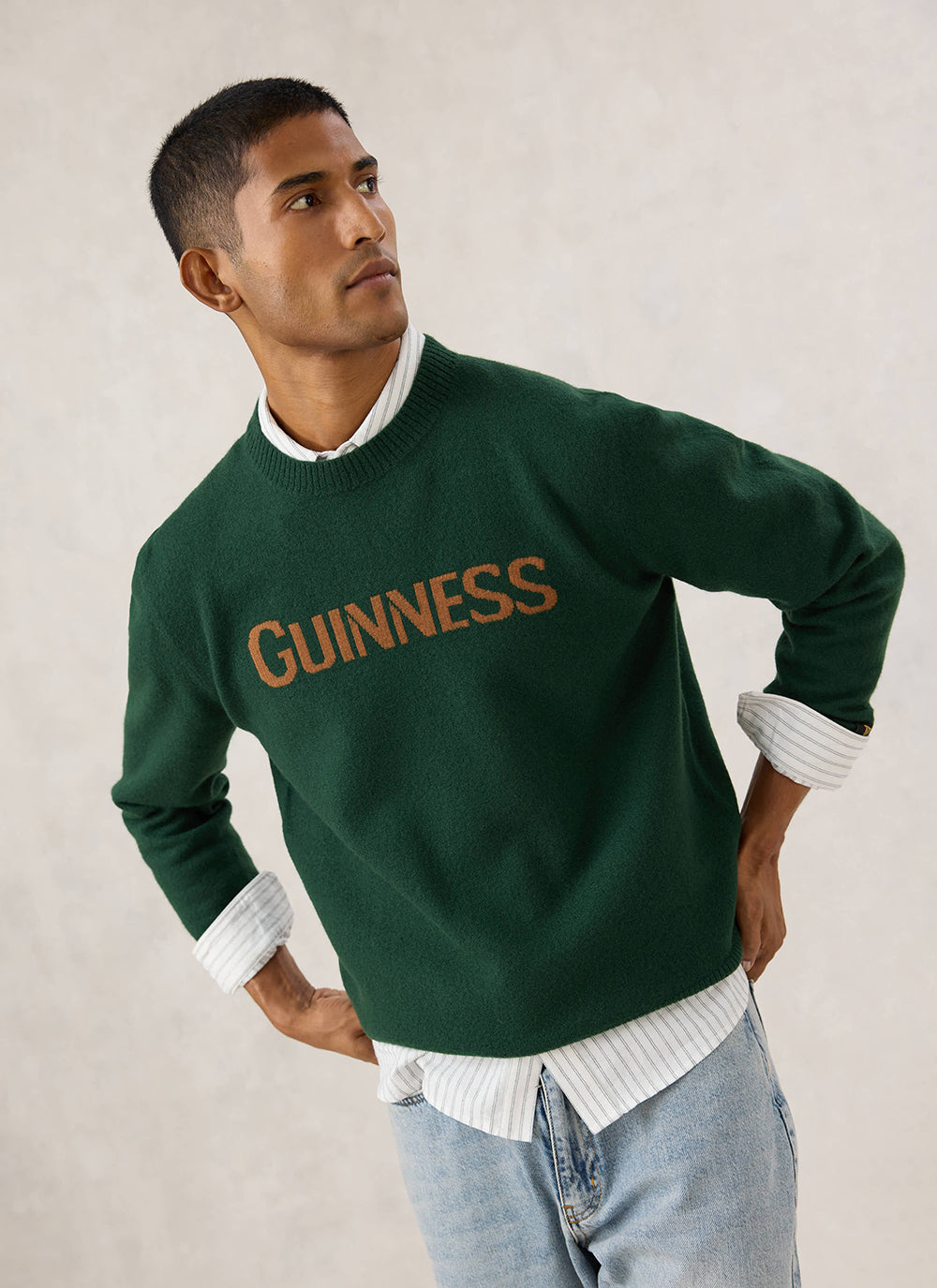 Model wearing the Guinness x Percival forest green merino wool jumper with bold jacquard lettering across the chest.