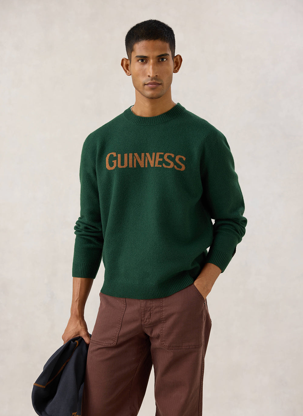 Model wearing the Guinness x Percival forest green merino wool jumper, featuring the bold contrasting jacquard chest logo.